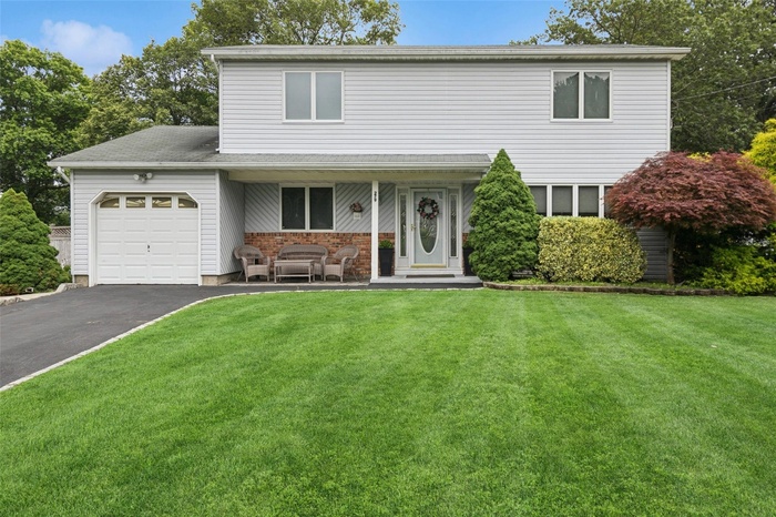 Traditional-style house with an attached garage, a front lawn, driveway, and brick siding