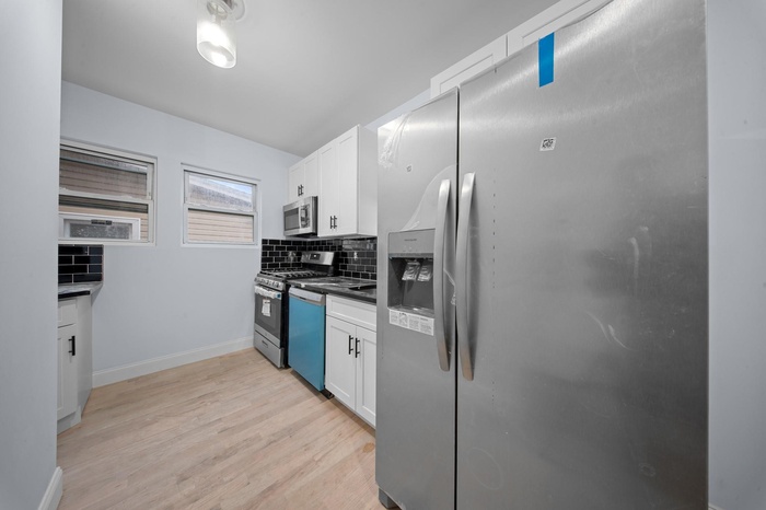 Kitchen with appliances with stainless steel finishes, backsplash, white cabinetry, and light wood-type flooring