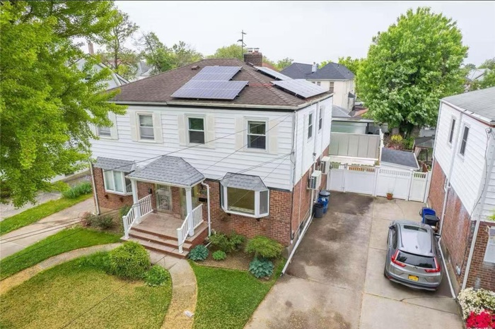 View of front of home featuring brick siding, a shingled roof, solar panels, a chimney, and a porch