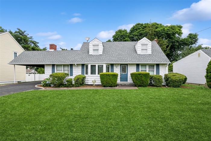 Cape cod-style house with a shingled roof, a chimney, a front lawn, and asphalt driveway