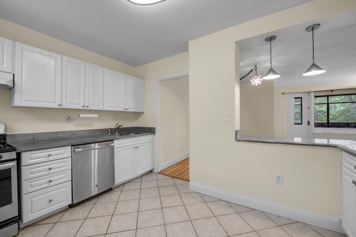 Kitchen with stainless steel appliances, white cabinetry, light tile patterned floors, decorative light fixtures, and dark stone counters
