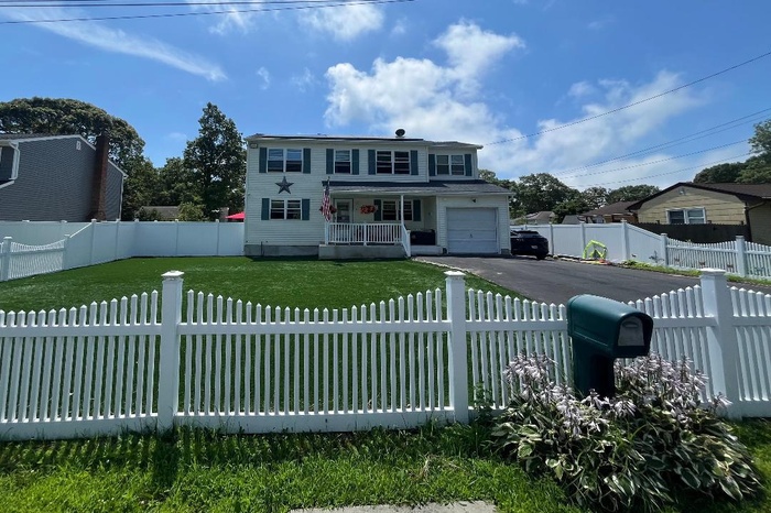 Traditional-style house featuring covered porch, asphalt driveway, a fenced front yard, and a garage