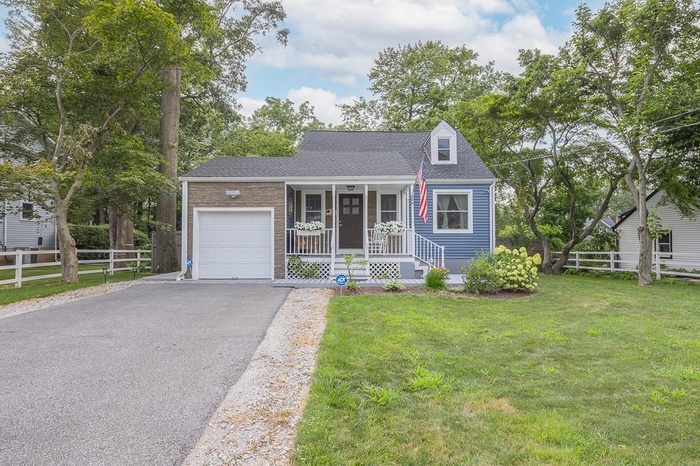 Cape cod home with a garage, driveway, roof with shingles, and a porch