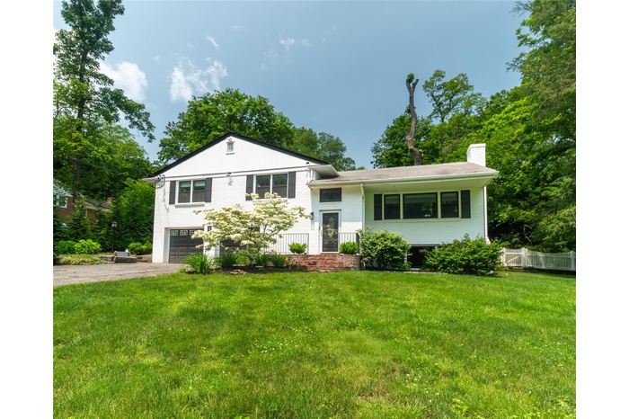 Tri-level home featuring driveway, a garage, a chimney, and brick siding
