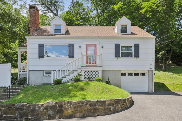 Cape cod home with a garage, a chimney, and a front lawn