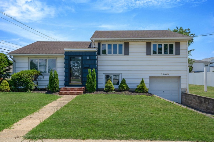Tri-level home featuring roof with shingles, a garage, and driveway