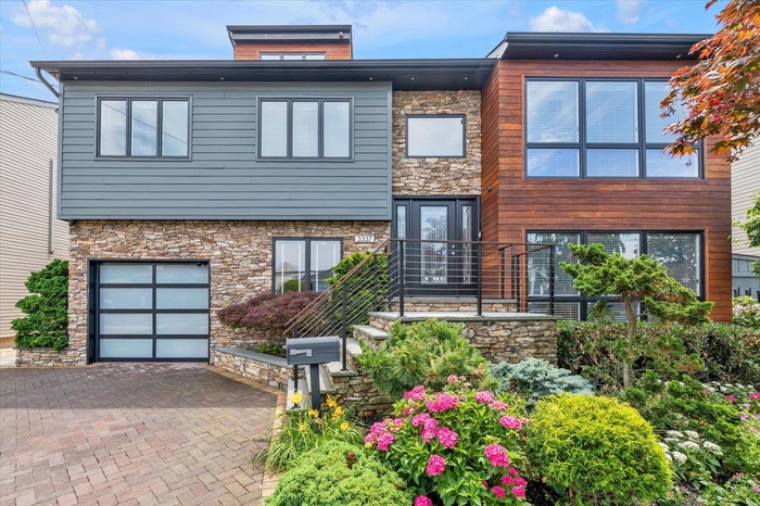 Contemporary house with stone siding, a garage, and decorative driveway
