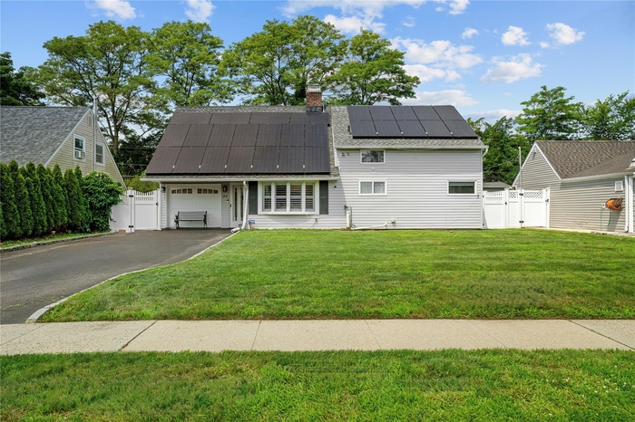 View of front of property featuring a gate, solar panels, asphalt driveway, and a garage
