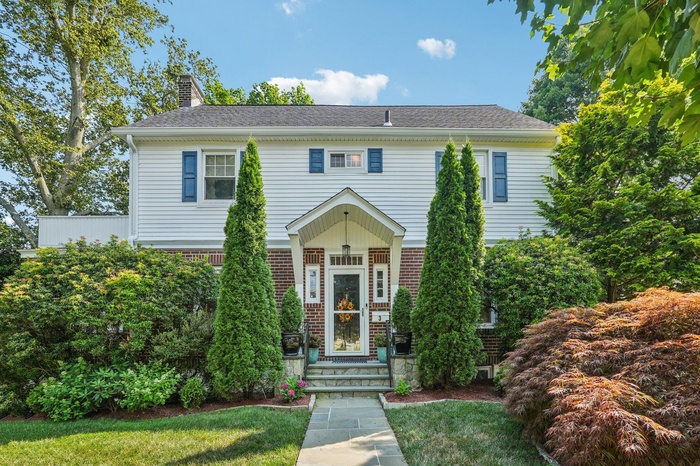 View of front facade with a chimney, brick siding, a front lawn, and a shingled roof