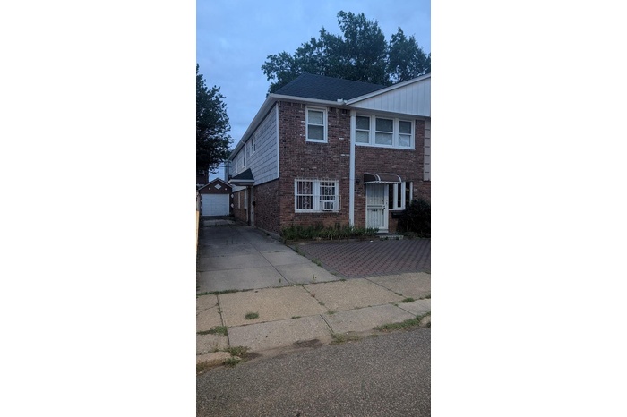 View of front of property featuring brick siding, a garage, an outdoor structure, and a shingled roof