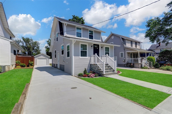 Traditional home with concrete driveway, an outbuilding, a detached garage, a porch, and a front lawn