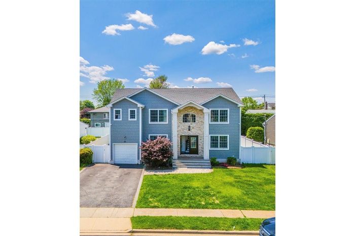 View of front of house with asphalt driveway, an attached garage, stone siding, and roof with shingles