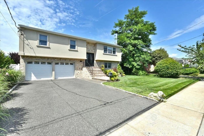 Bi-level home with stucco siding, driveway, an attached garage, a front lawn, and stone siding
