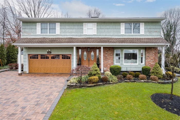 View of front of house with an attached garage, a shingled roof, a front yard, and decorative driveway