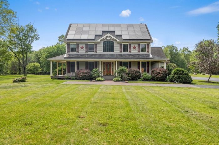 View of front facade with a porch, a front yard, and roof mounted solar panels