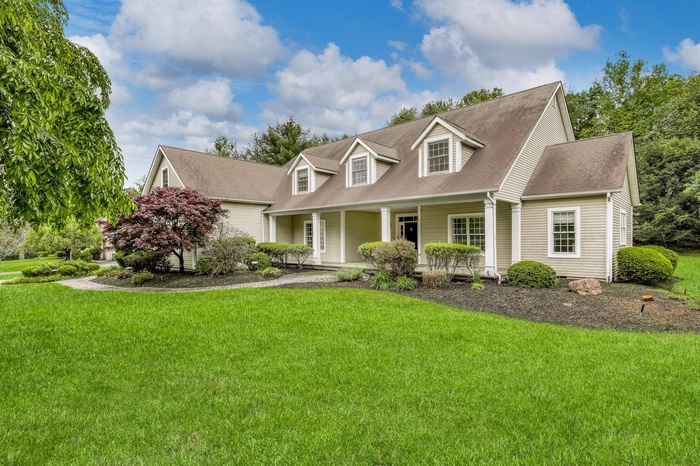 New england style home featuring a porch, a front lawn, and a shingled roof