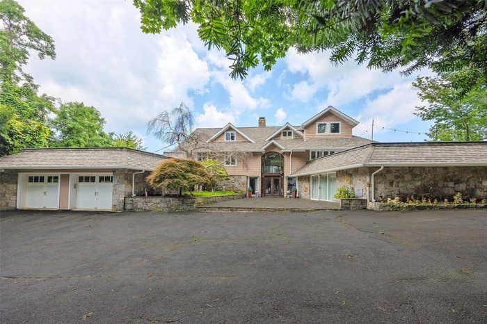 View of front of home featuring stone siding, a chimney, driveway, and a garage