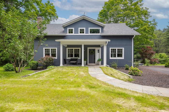 View of front facade with a porch, a shingled roof, a chimney, and a front lawn