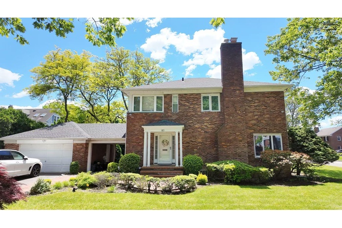 View of front of property featuring an attached garage, a chimney, brick siding, and a front yard
