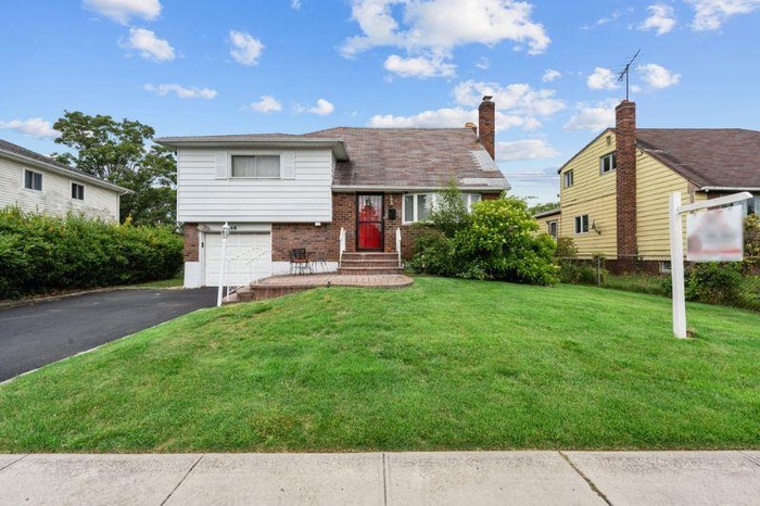 Tri-level home with brick siding, a front lawn, a garage, and asphalt driveway