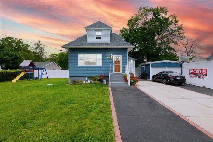 View of front of house featuring roof with shingles, a playground, a garage, and an outbuilding