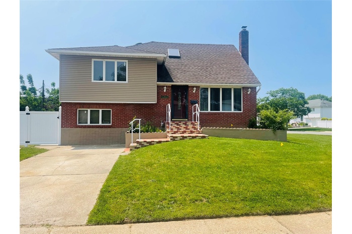 Split level home featuring brick siding, a chimney, a gate, and roof with shingles