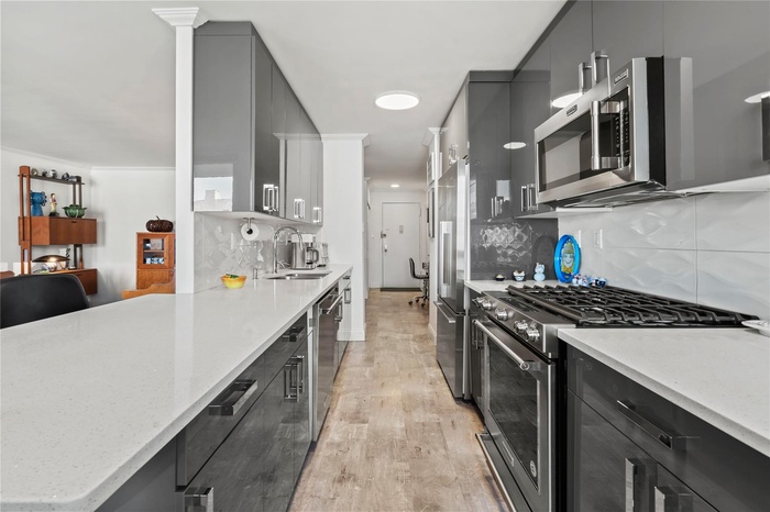 Kitchen with light hardwood / wood-style floors, sink, tasteful backsplash, light stone counters, and high quality appliances