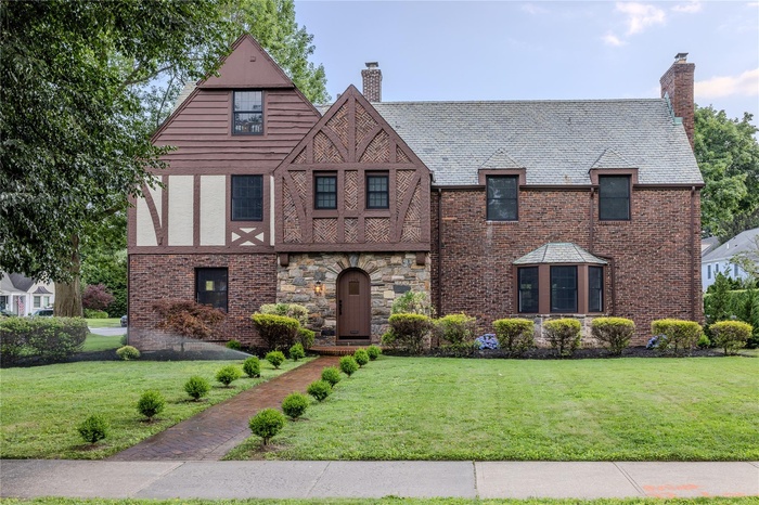 Tudor home featuring a chimney, a front lawn, a high end roof, and brick siding