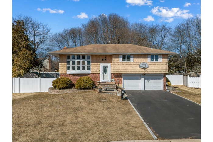 Bi-level home featuring aphalt driveway, brick siding, an attached garage, fence, and a front lawn