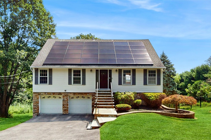 View of front facade with driveway, a front yard, solar panels, and a garage