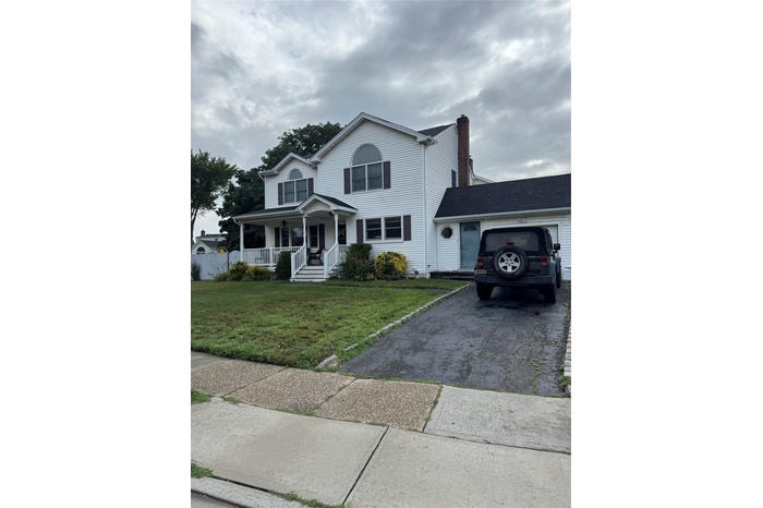View of front facade featuring asphalt driveway, covered porch, an attached garage, and a front yard