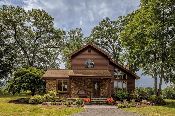 Rustic home featuring stone siding, a front lawn, and a shingled roof