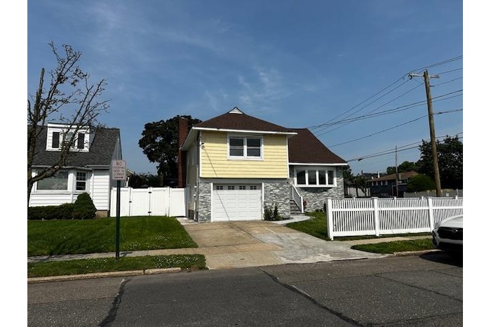 View of front of home with stone siding, a garage, driveway, a gate, and a chimney
