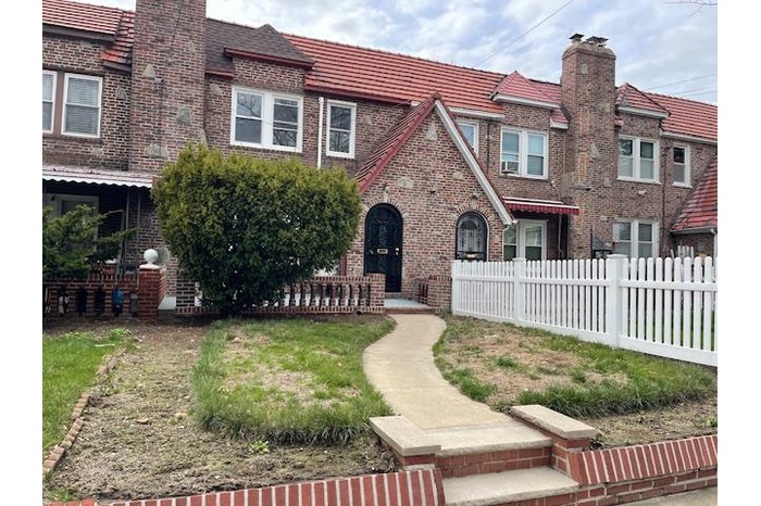 View of front of home with brick siding, fence, and a chimney