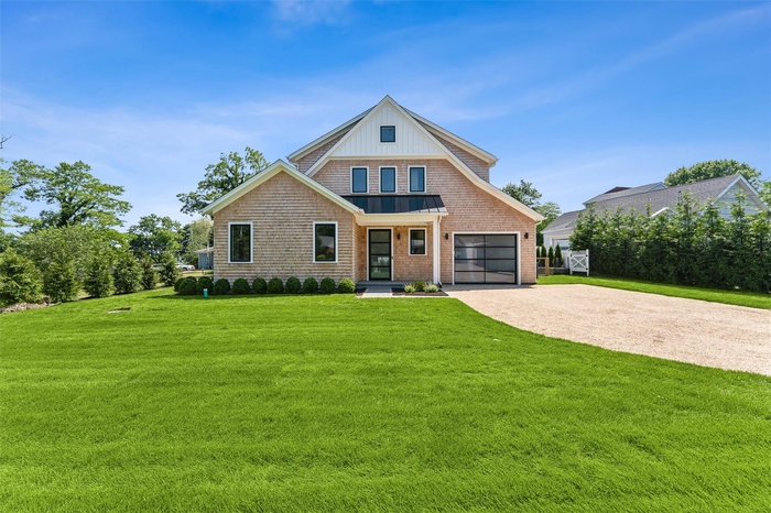 View of front facade featuring driveway, a standing seam roof, a front lawn, a metal roof, and an attached garage
