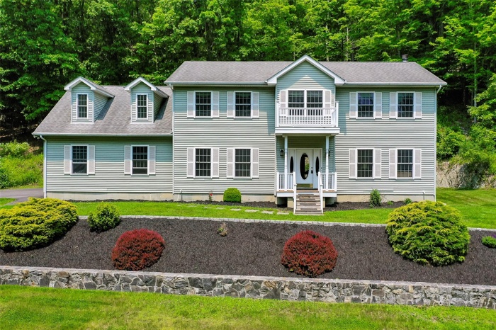 View of front facade with a balcony, a front lawn, and roof with shingles