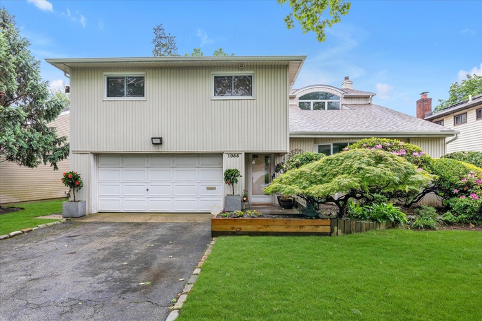Tri-level home with asphalt driveway, an attached garage, a front lawn, a chimney, and roof with shingles