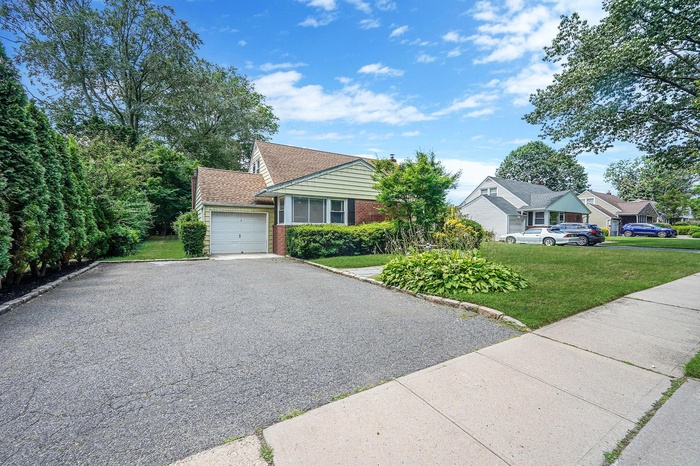 View of front facade featuring driveway, an attached garage, a front yard, and brick siding