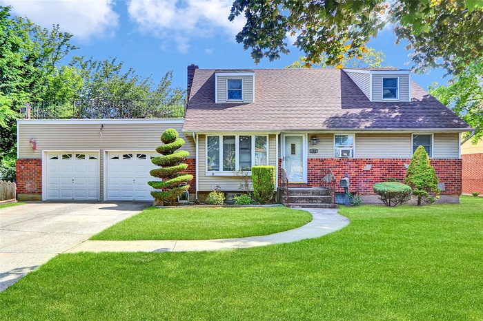 Cape cod-style house with concrete driveway, a garage, a front yard, a shingled roof, and a chimney