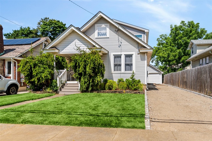 View of front of property with a front lawn, a porch, an outdoor structure, and a garage