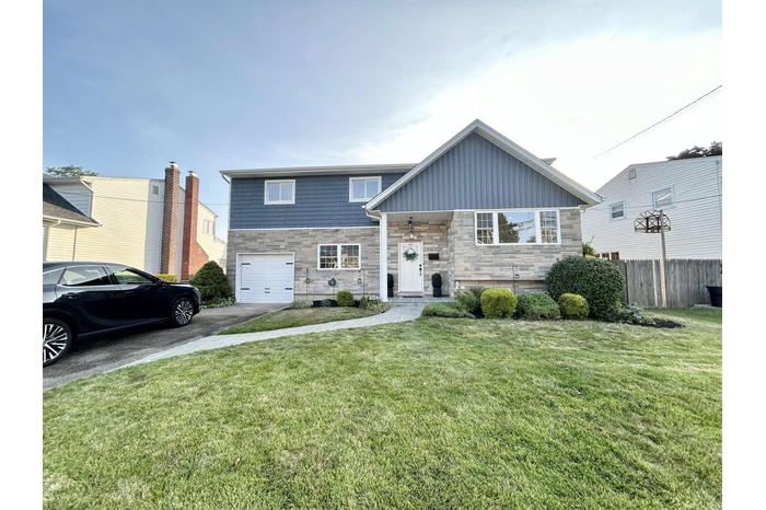 Split foyer home featuring stone siding, an attached garage, driveway, and board and batten siding