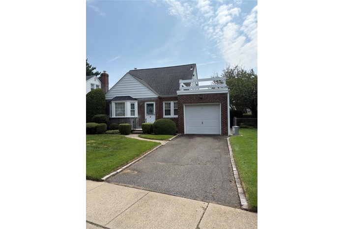 View of front facade with roof with shingles, asphalt driveway, brick siding, and a garage