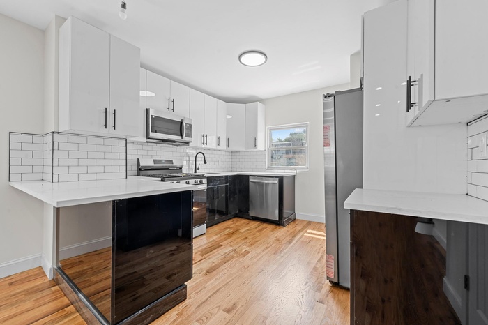 Kitchen with stainless steel appliances, light wood-type flooring, tasteful backsplash, and white cabinetry