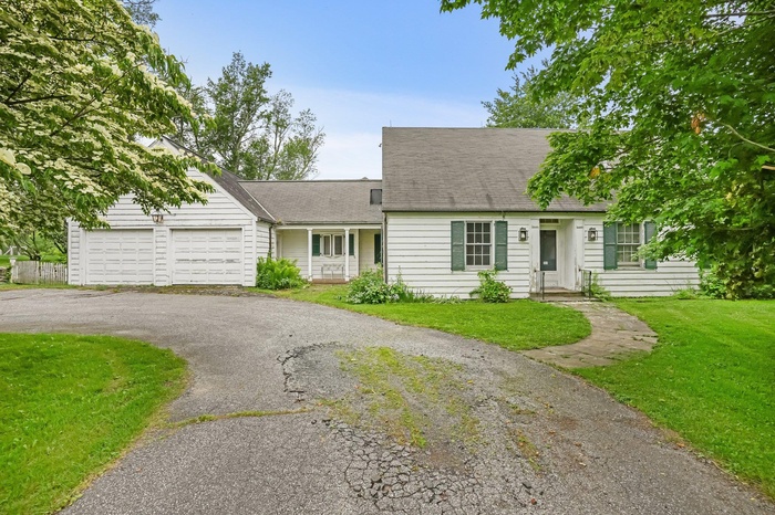 Cape cod house with an attached garage, a front yard, asphalt driveway, and roof with shingles