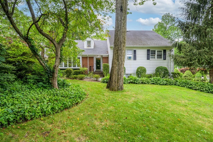 View of front facade featuring a front lawn, a shingled roof, and brick siding