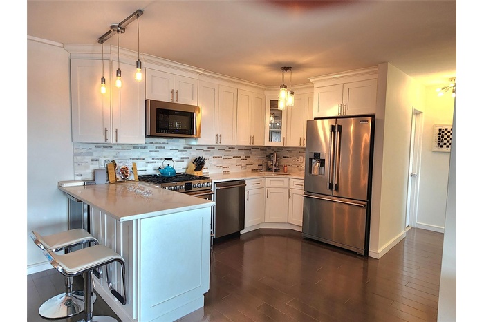 Kitchen with light countertops, white cabinetry, a peninsula, stainless steel appliances, and decorative backsplash
