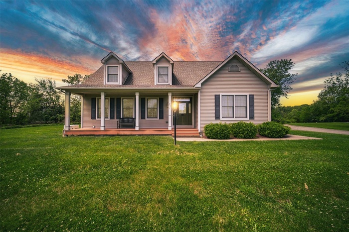 View of front of property with a lawn, covered porch, and roof with shingles