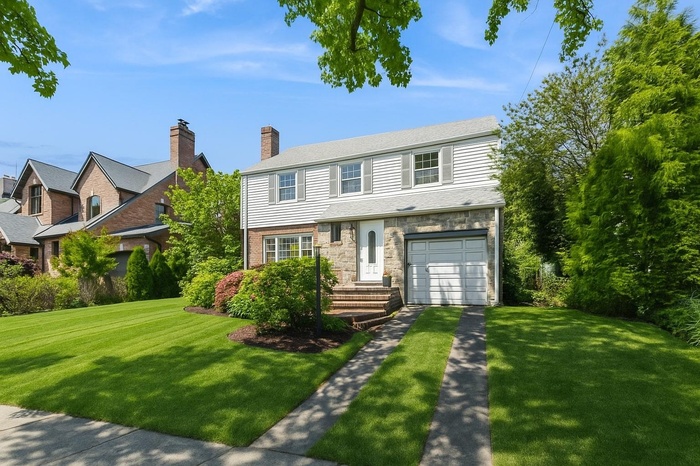View of front facade featuring concrete driveway, a front lawn, stone siding, and an attached garage