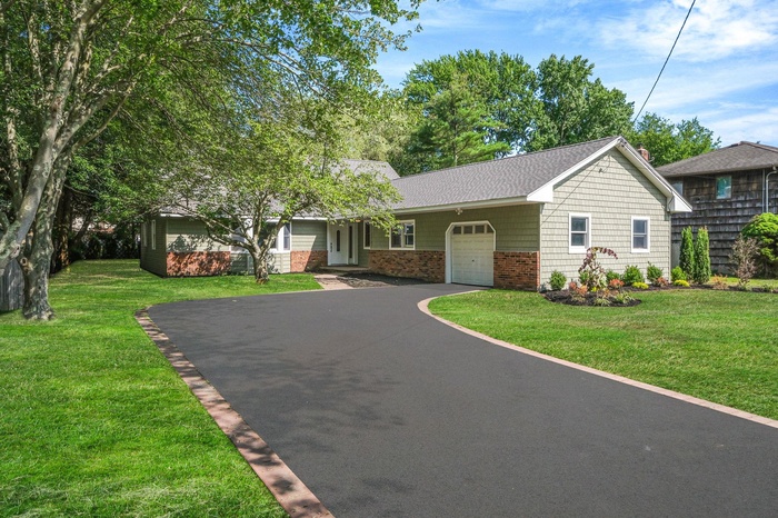 View of front of house featuring a garage, driveway, a front yard, roof with shingles, and brick siding