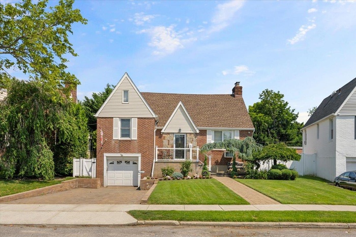 View of front of home with brick siding, decorative driveway, a garage, and a chimney